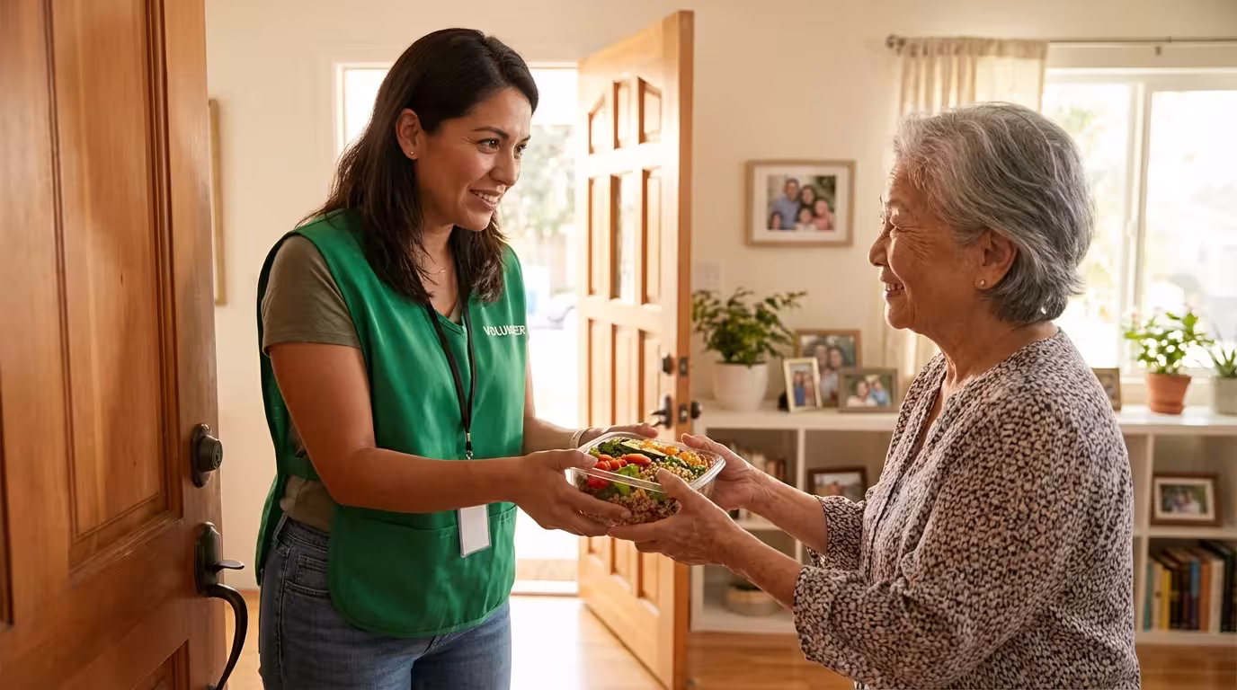 A friendly volunteer delivers a healthy prepared meal to a smiling senior woman at her home.