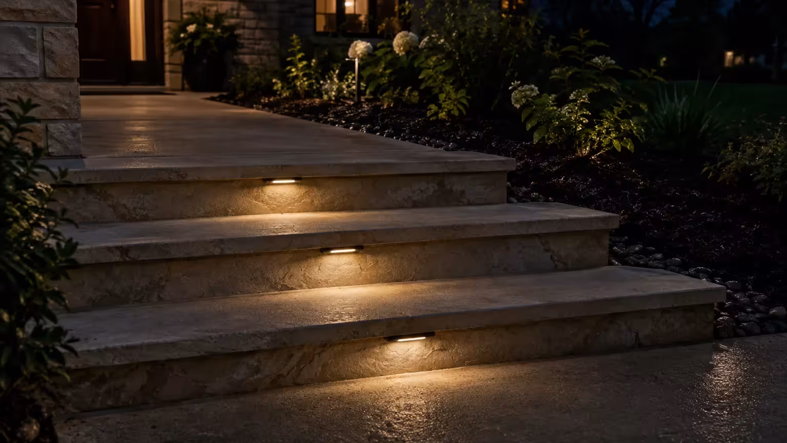Outdoor stone steps illuminated by warm horizontal lights integrated into each riser beside a garden bed at night.